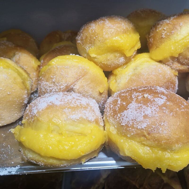 Bolas recheadas de creme amarelo e passadas por açúcar, na vitrina.