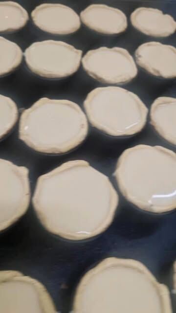 Formas de pastel de nata forradas de massa, ainda vazias, alinhadas num tabuleiro.