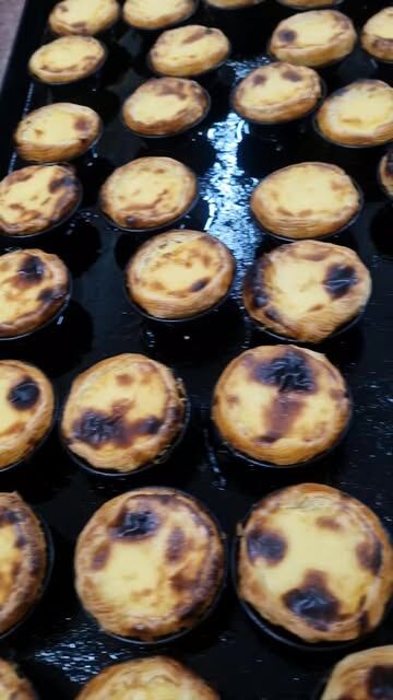 Um tabuleiro de pastéis de nata acabados de cozer, com o caramelo escuro por cima.