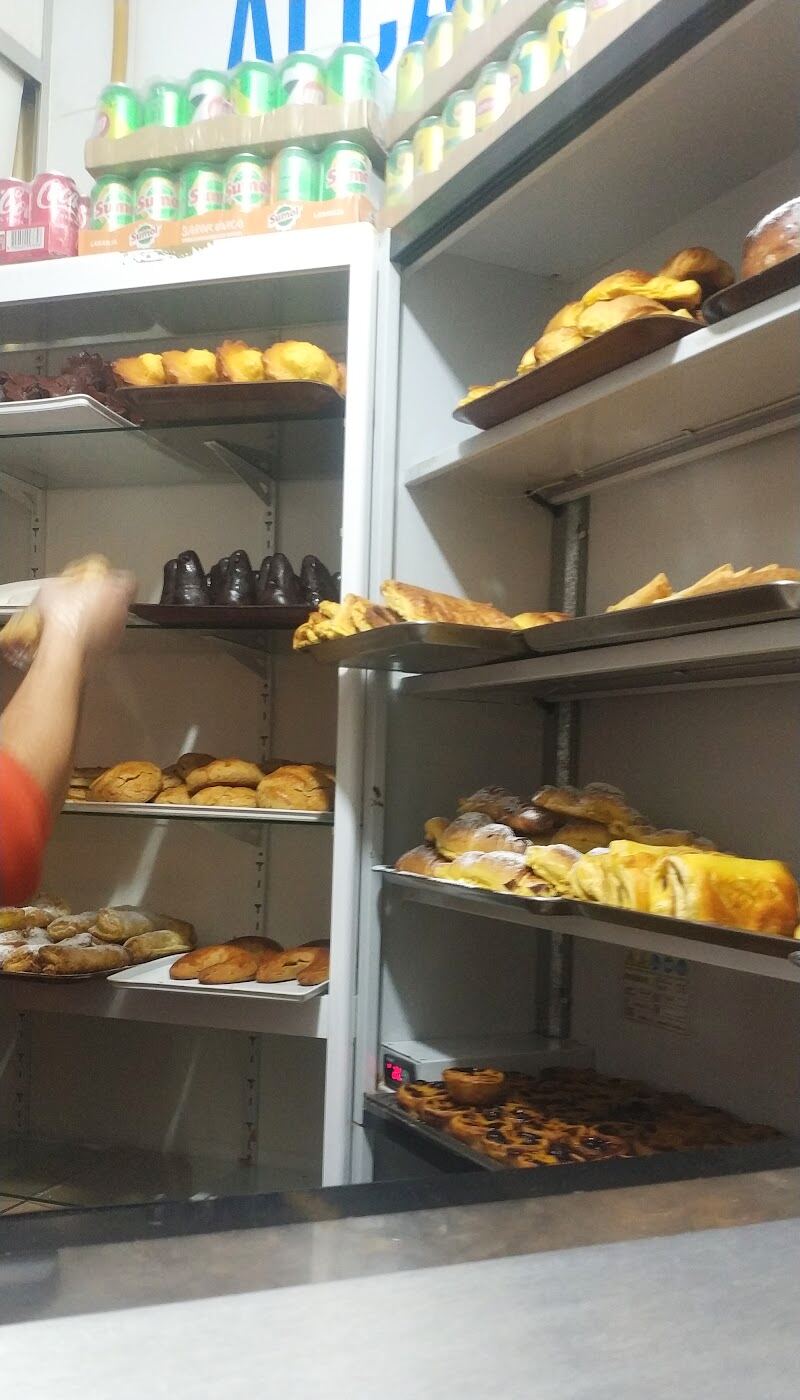 As prateleiras atrás do balcão cheias de bolos, de madrugada, com um pasteleiro a arrumar um tabuleiro.